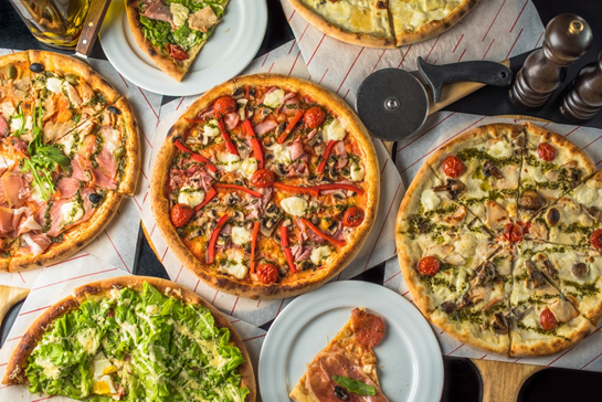 Various types of pizza with bright vegetables on top