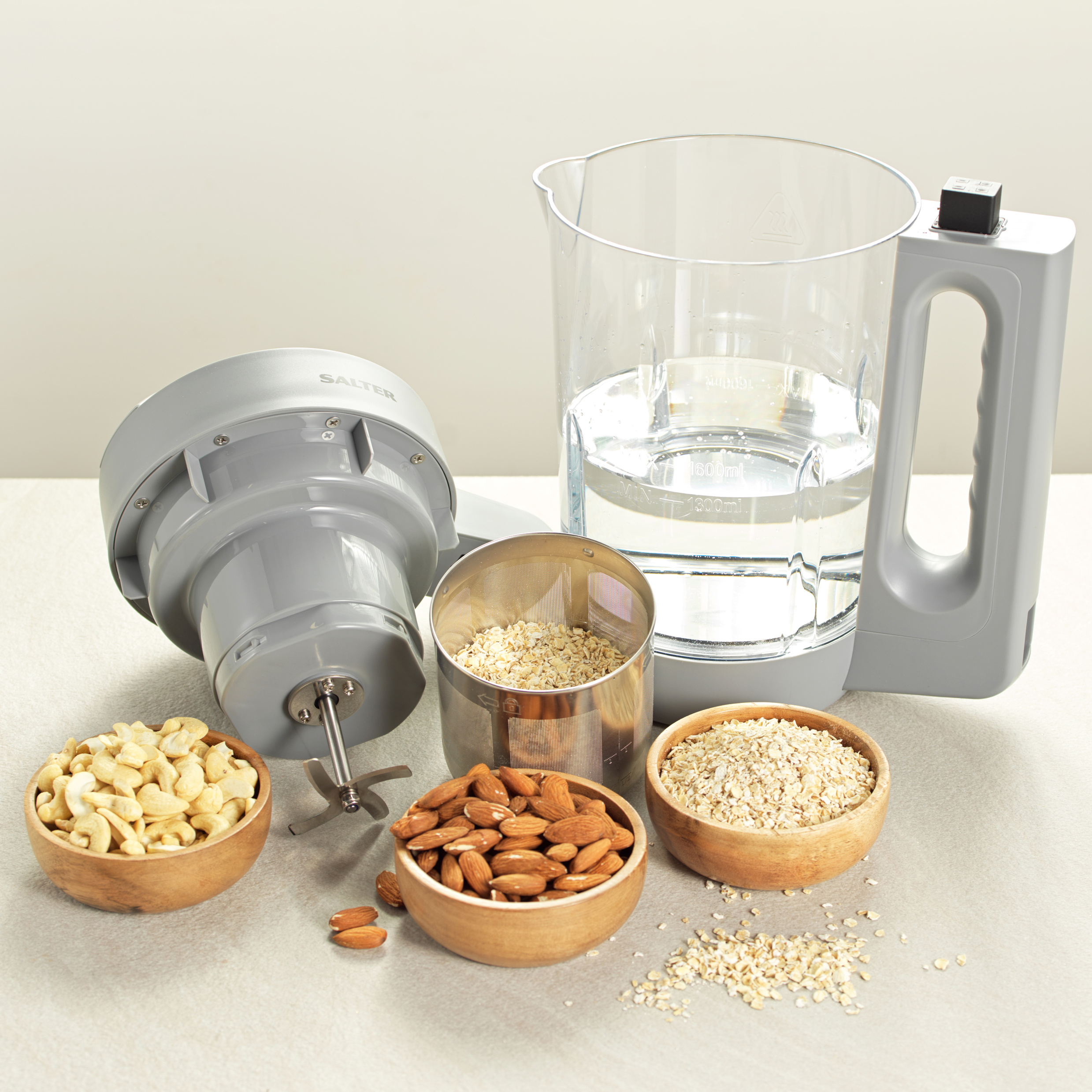 A plant milk maker with bowls of oats, nuts and almonds in front