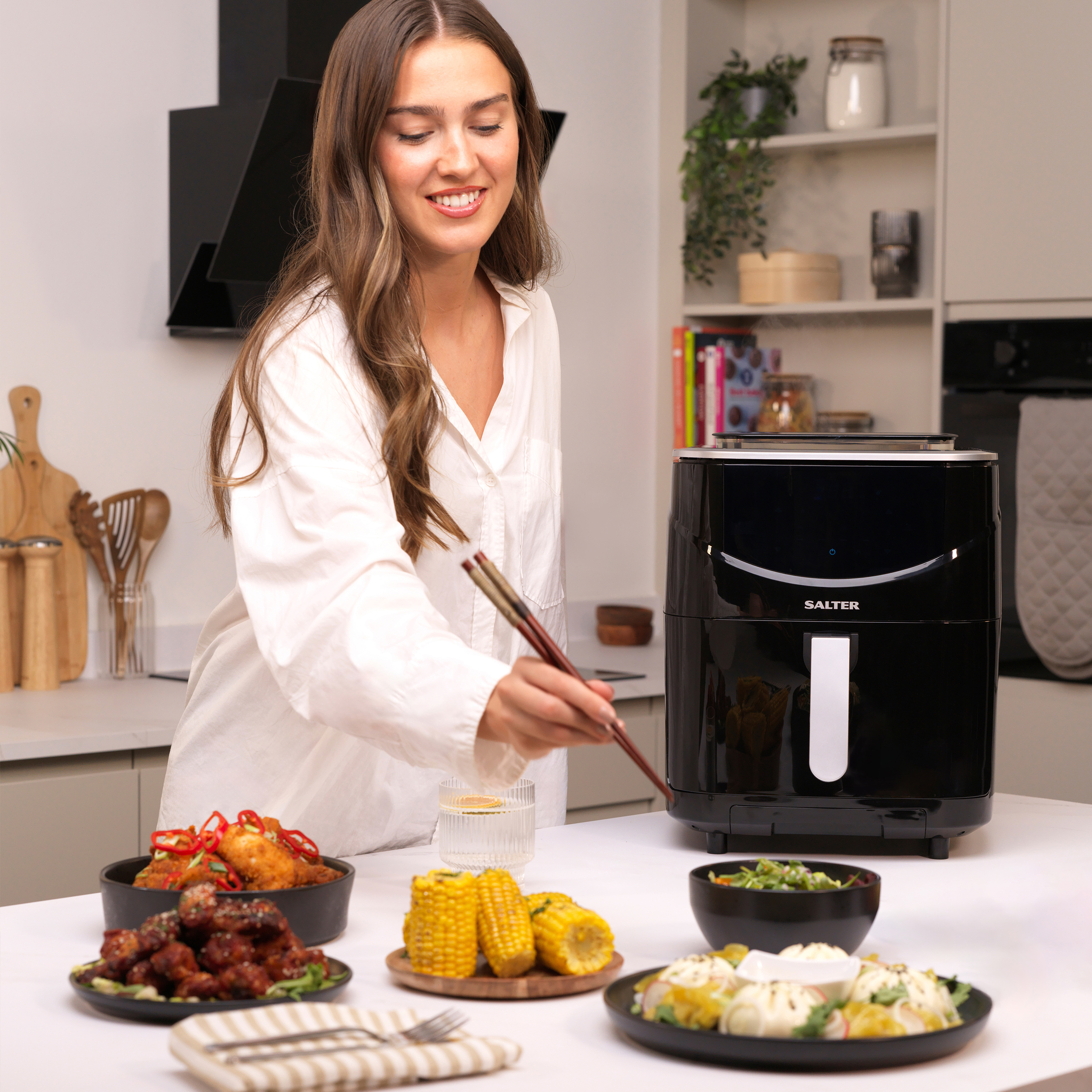 A woman reaching to eat food with Chopsticks in front of a Salter Fuzion Air Fryer